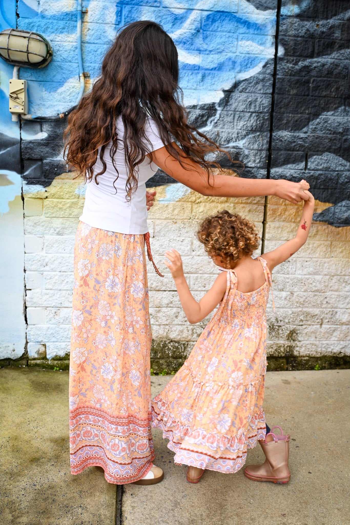 A woman and a young child walking hand in hand outdoors. The woman wears a white top and Mila Meli Lounge Pants Sunrise Botanica.