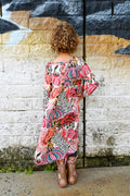 A woman with curly brown hair stands with her back to the camera, wearing a short-sleeve bohemian-style maxi dress Evie Dress Pink Agave Slub Rayon.