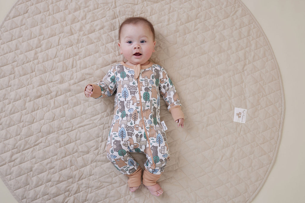 Baby lying on a quilted surface wearing Aster & Oak Organic Zip – Noah Woodland Onesie.