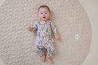 Baby lying on a quilted surface wearing Aster & Oak Organic Zip – Noah Woodland Onesie.