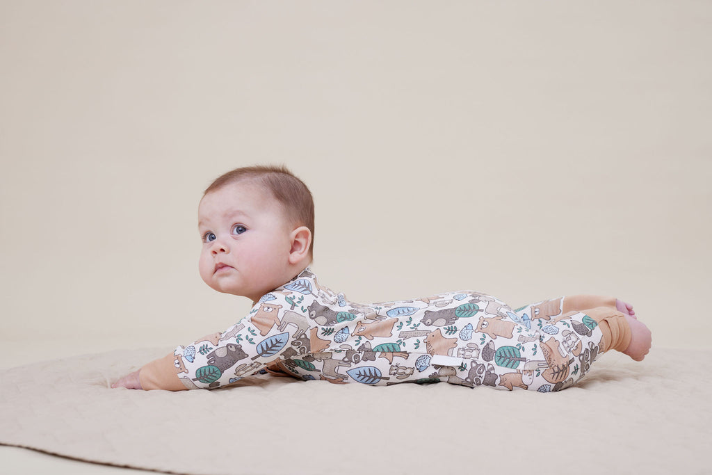 Baby lying on a quilted surface wearing Aster & Oak Organic Zip – Noah Woodland Onesie.