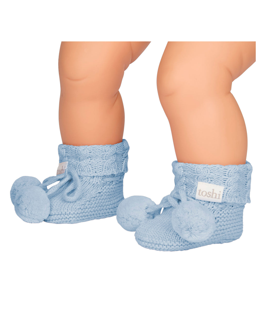 Baby's feet wearing Bluebell, a light blue organic baby booties with pom-pom on a white background.