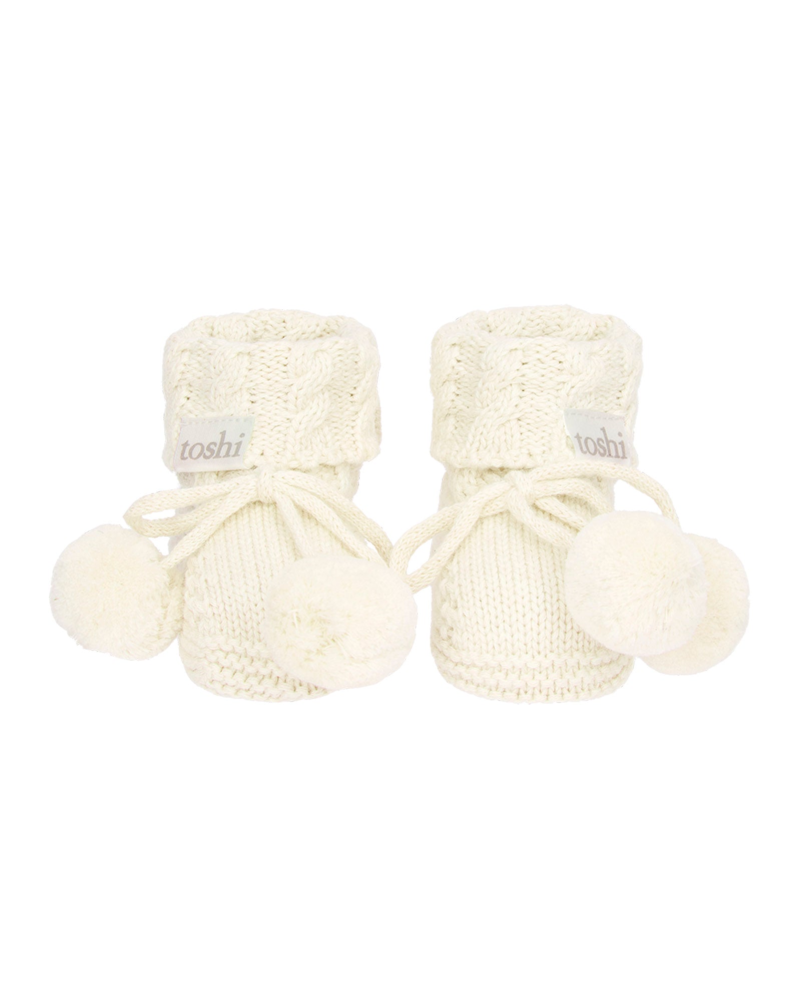 Pair of cream baby booties with pom-poms on a white background