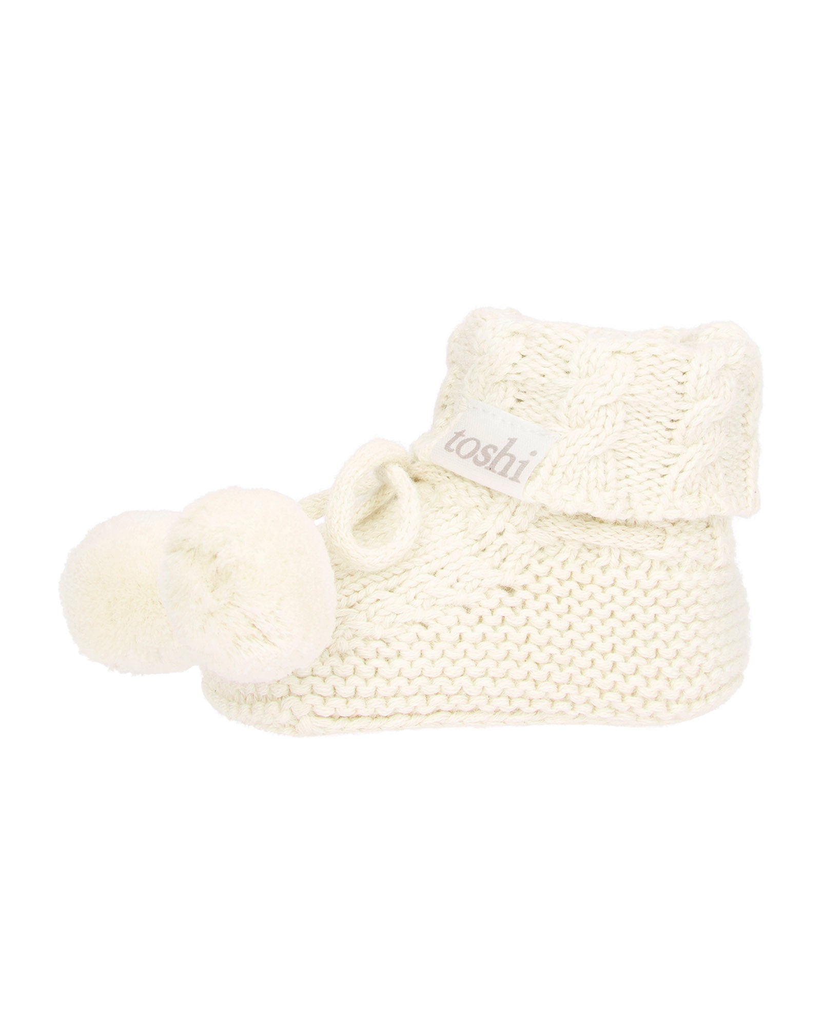 cream knitted baby booties with pom-pom on a white background