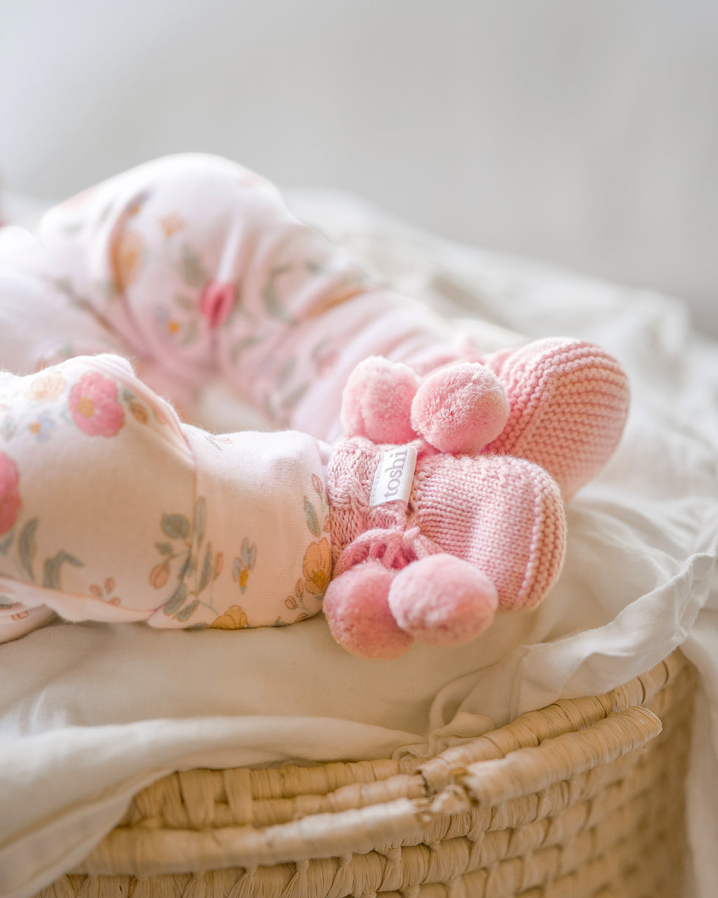 Pink knitted booties with pom-poms and 'toshi' branding on a white background