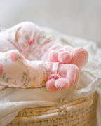 Pink knitted booties with pom-poms and 'toshi' branding on a white background