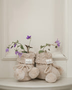 Flowers on beige knitted booties with pom-poms and 'toshi' branding on a light cream background