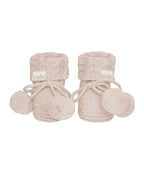 Oatmeal, a Pair of beige knitted baby booties with pom-poms on a white background.