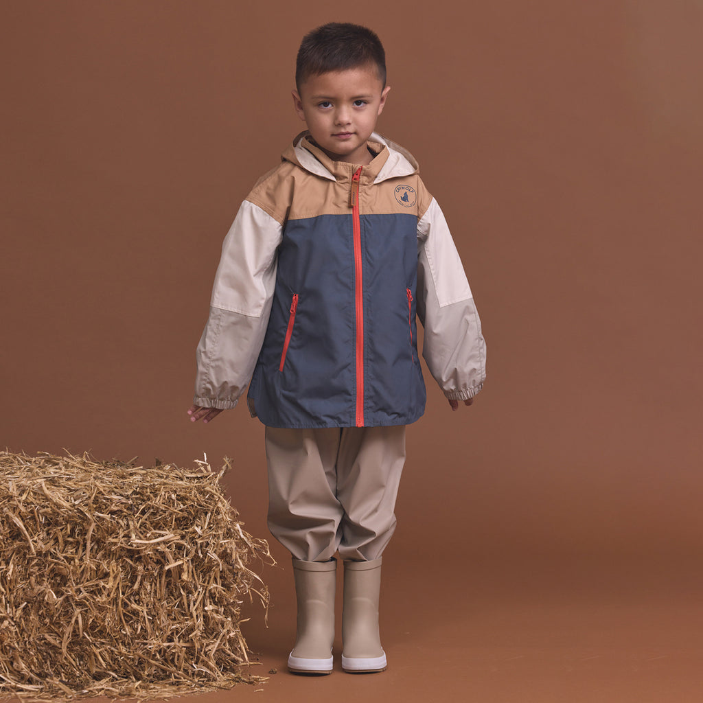 Child wearing the Crywolf Packable Jacket Ash Colourblock and pants standing next to a bale of hay on a brown background