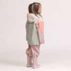 Child wearing a Color-blocked kids' waterproof jacket featuring an off-white upper body and hood, a sage green central torso, and terracotta pink sleeves with a cream zipper, pink pants and Crywolf Rain Boots Dusty Pink on a light background.
