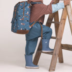 Person wearing a blue raincoat, pants, and boots with a backpack wearing a pair of Rain Boots Highland Blue. 
