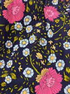 A close-up of a dark navy floral fabric with large pink flowers, small light blue daisies with yellow centers, and green leaves and stems.