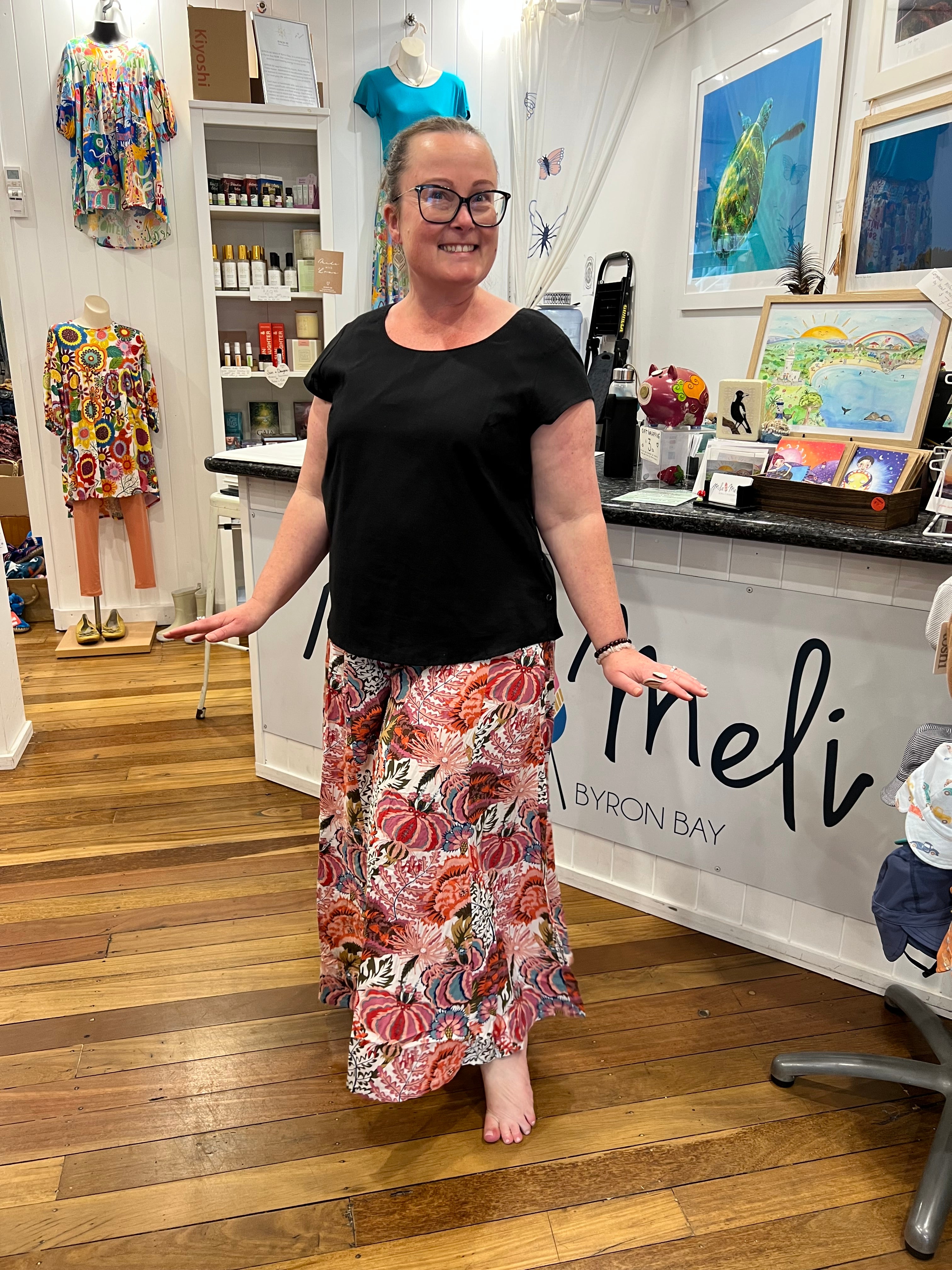 A woman wearing a black short-sleeve top and a long, wide Byron Pant Agave Pinks.