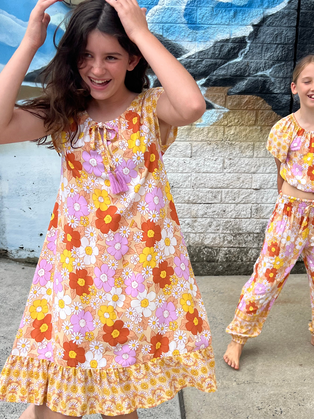 Two young girls in matching Sundaisy print, a vintage floral pattern in mustard yellow, rust orange, and dusty pink.