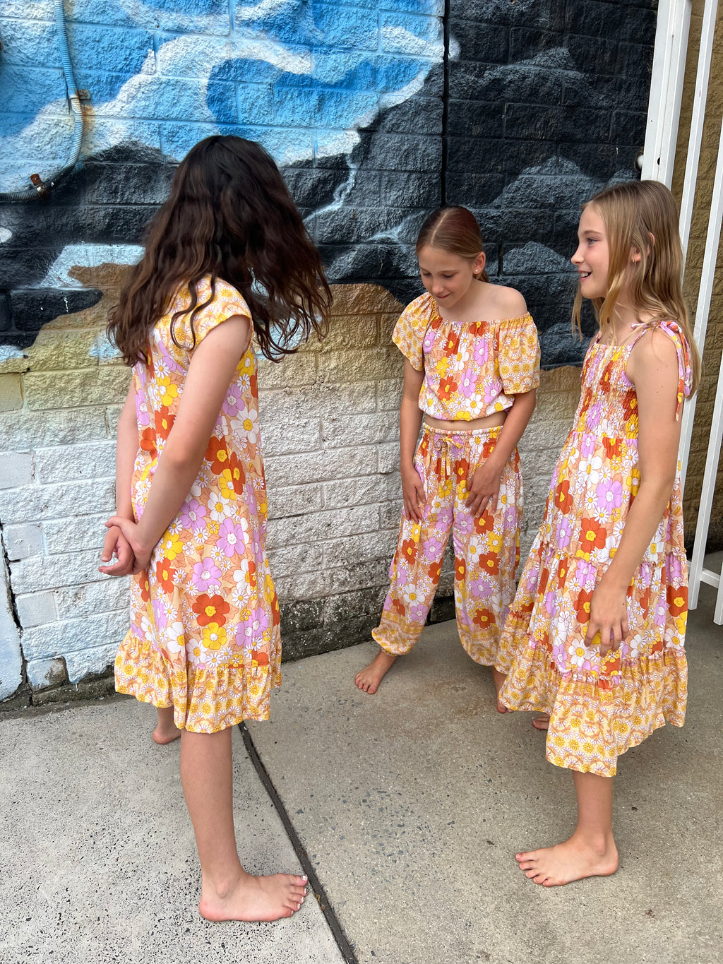 Three young girls in matching Sundaisy print, a vintage floral pattern in mustard yellow, rust orange, and dusty pink.