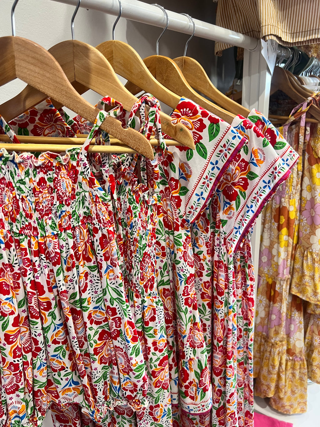Floral dress featuring Fiesta Bloom print, a white base with a vibrant floral pattern in red, orange, green, and blue on hangers in a store setting