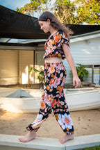 Girl wearing a black two-piece set featuring a short-sleeve top and wide-leg pants with Wild Dahlia print, a bold retro floral print in warm orange, mustard, and peach.