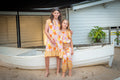 Two young girls in matching Sundaisy prints, a vintage floral pattern in mustard yellow, rust orange, and dusty pink.  On Left wearing the Sundaisy Frill dress while on right the girl wearing Sundaisy Lil Watego pants and blouse.