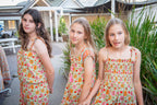 Three young girls wearing a Festival Garden print, a white base with an all-over floral pattern of orange, pink, and green.