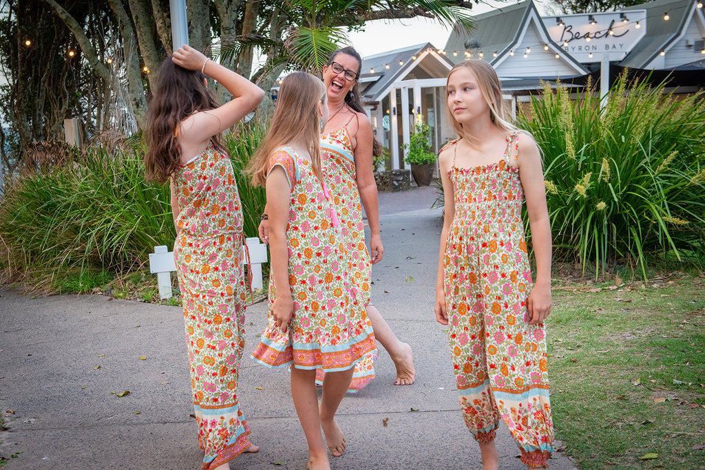 Three young girls wearing a Festival Garden print, a white base with an all-over floral pattern of orange, pink, and green.