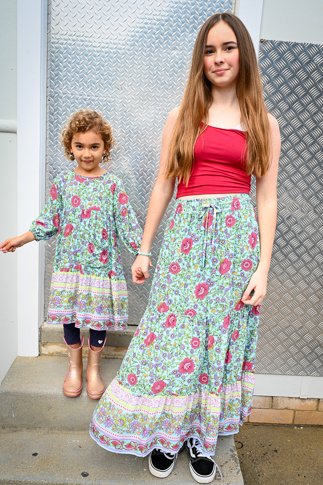 A woman and a young girl standing on concrete steps. The woman wears a sleeveless red top and a long Maeve Maxi Skirt Aqua Wildflower.