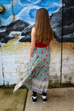 A woman with long brown hair stands with her back to the camera, wearing a Maeve Maxi Skirt Aqua Wildflower.