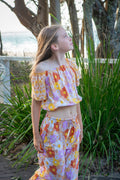Young girl in wearing two piece set of  Sun Daisy print, a vintage floral pattern in mustard yellow, rust orange, and dusty pink, featuring a smocked elastic top, adjustable shoulder ties, and wide-leg trousers.