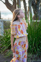 Young girl in wearing two piece set of  Sun Daisy print, a vintage floral pattern in mustard yellow, rust orange, and dusty pink, featuring a smocked elastic top, adjustable shoulder ties, and wide-leg trousers.