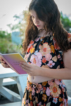 Girl wearing a black two-piece set featuring a short-sleeve top and wide-leg pants with Wild Dahlia print, a bold retro floral print in warm orange, mustard, and peach.