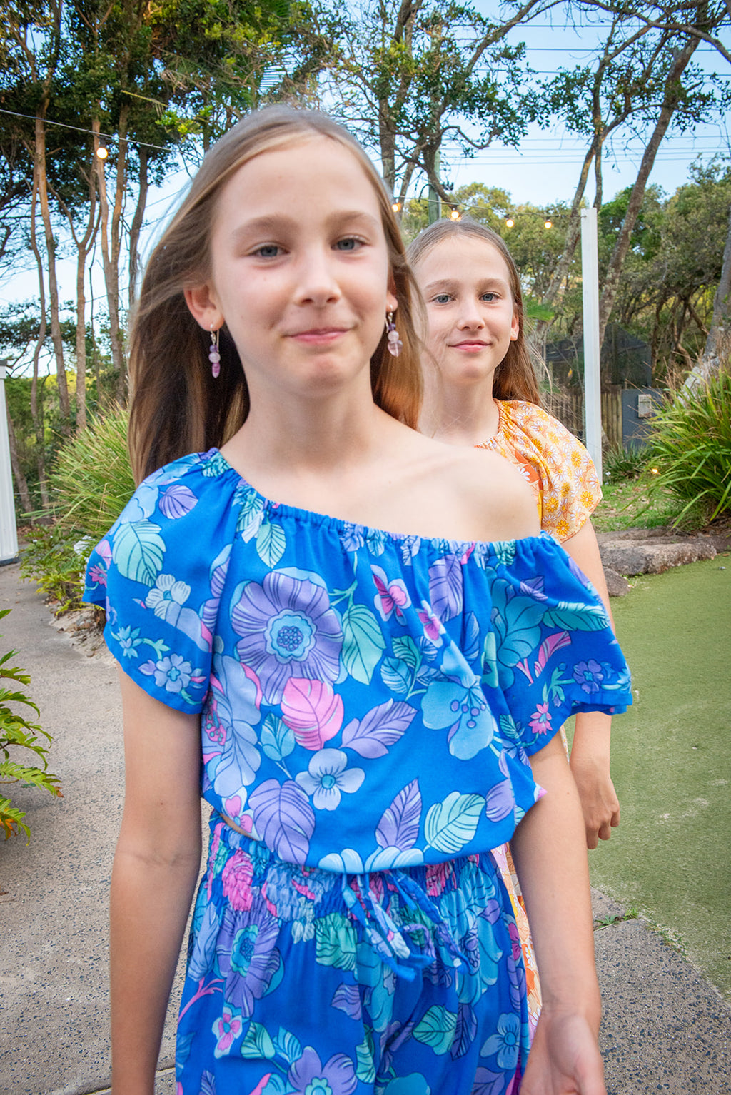 Kid wearing a bohemian-style outfit consisting of Lapiz Dahlia, a blue short-sleeve crop top and matching trousers decorated with a colorful floral pattern.