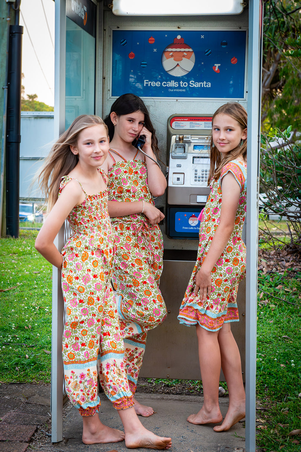Three young girls in MilaMeli Festival Garden print clothes, standing in front of a phone booth.