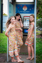 Three young girls in MilaMeli Festival Garden print clothes, standing in front of a phone booth.