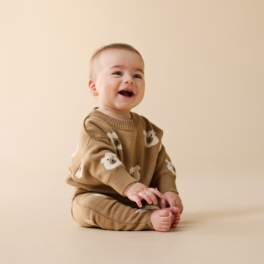 Baby wearing a Wilson & Frenchy Organic Knitted Jacquard Jumper a brown sweater with bear patterns.