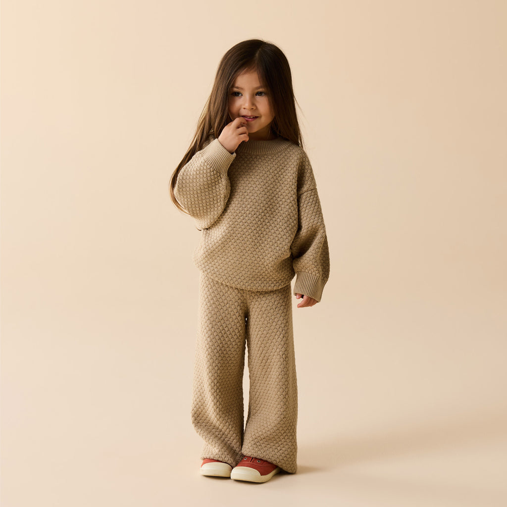 Child wearing a beige textured sweater and pants set on a beige background