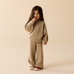 Child wearing a beige textured sweater and pants set on a beige background