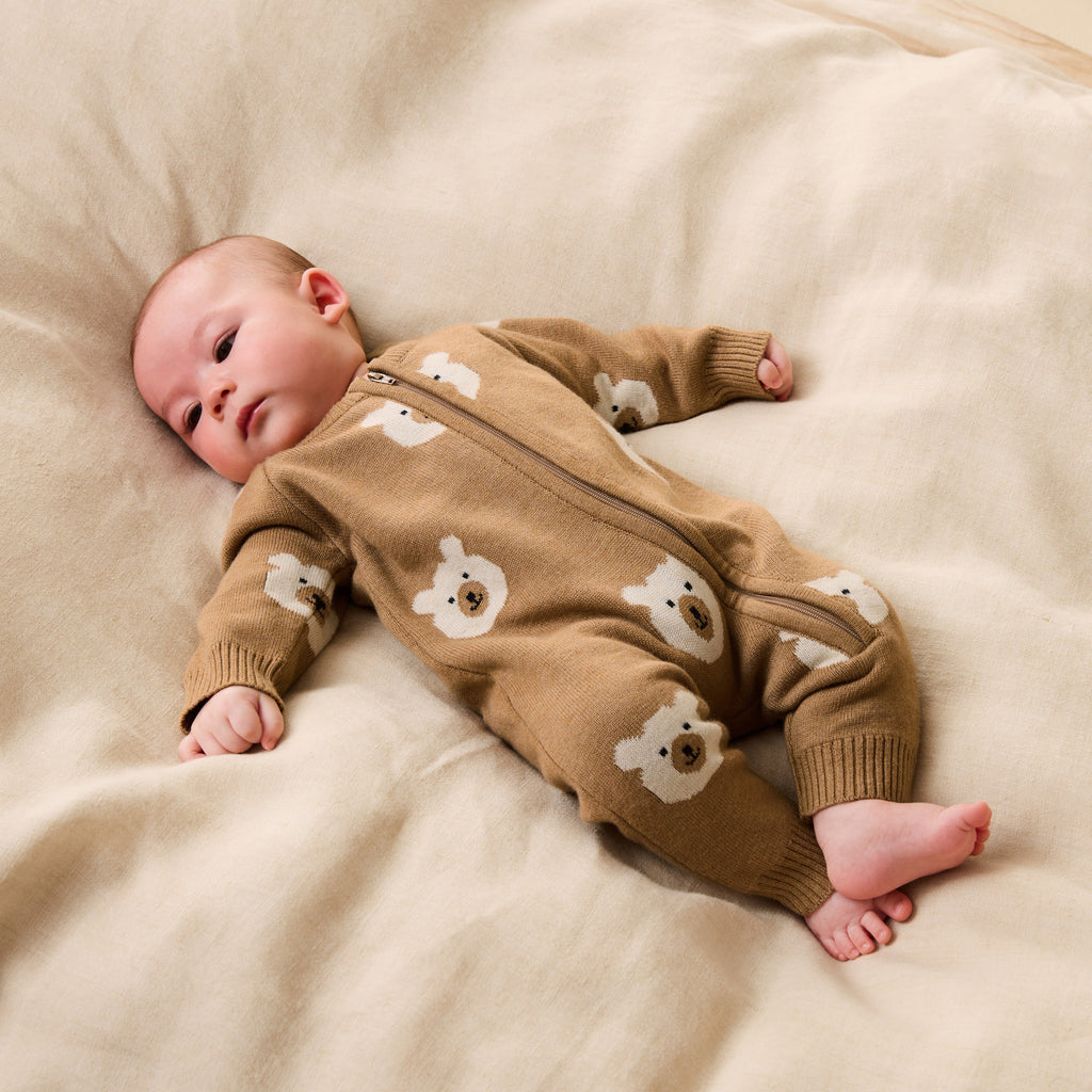 Baby wearing a Wilson & Frenchy Organic Knitted Jacquard Growsuit, a brown onesie with bear patterns while lying on a beige blanket