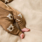 Baby wearing a Wilson & Frenchy Organic Knitted Jacquard Growsuit, a brown onesie with bear patterns while lying on a beige blanket