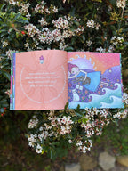 Open book with colorful illustrations and text, surrounded by flowers and greenery