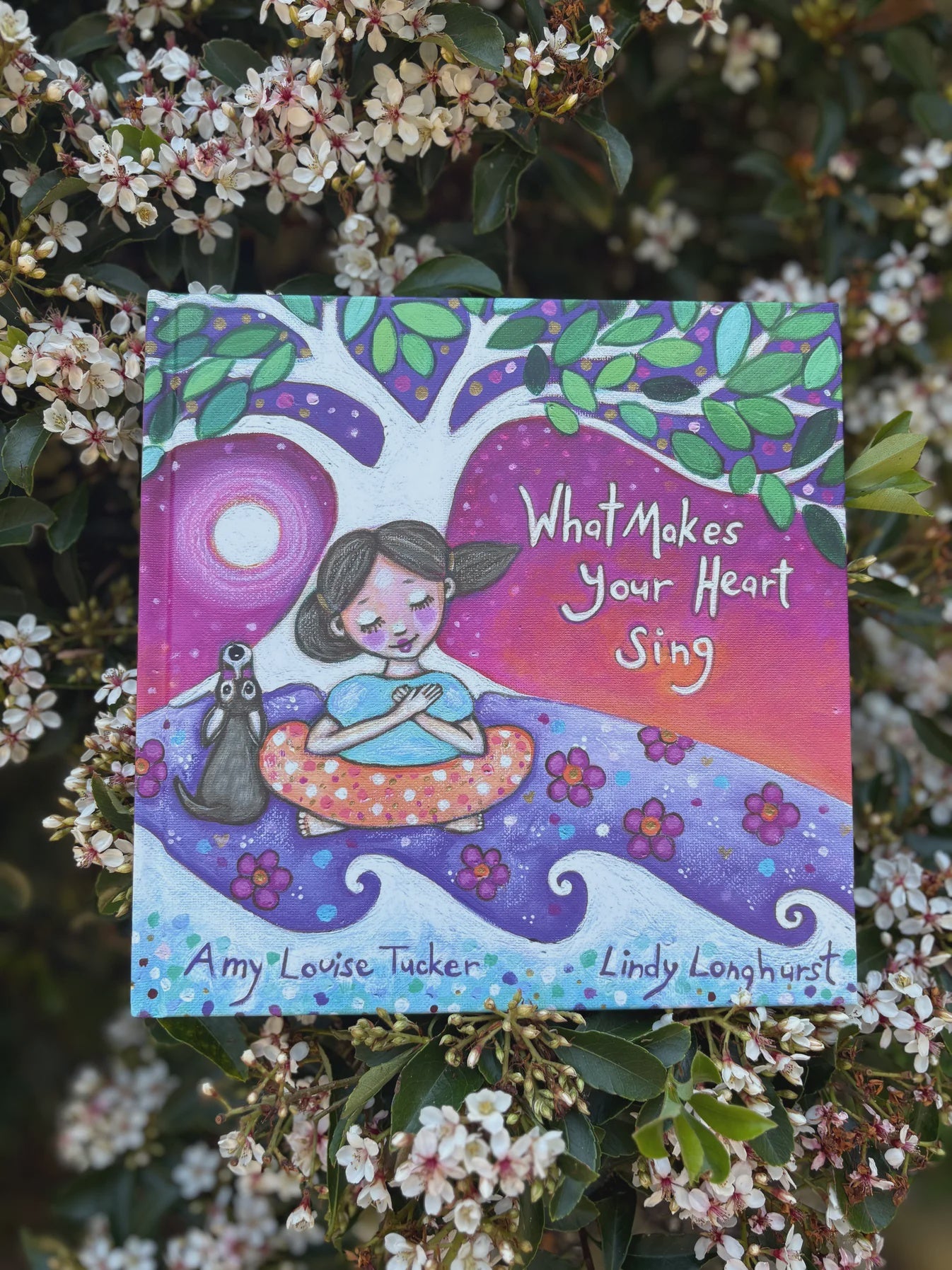 Book titled 'What Makes Your Heart Sing' by Amy Louise Tucker and Lindy Longhurst, surrounded by flowers.