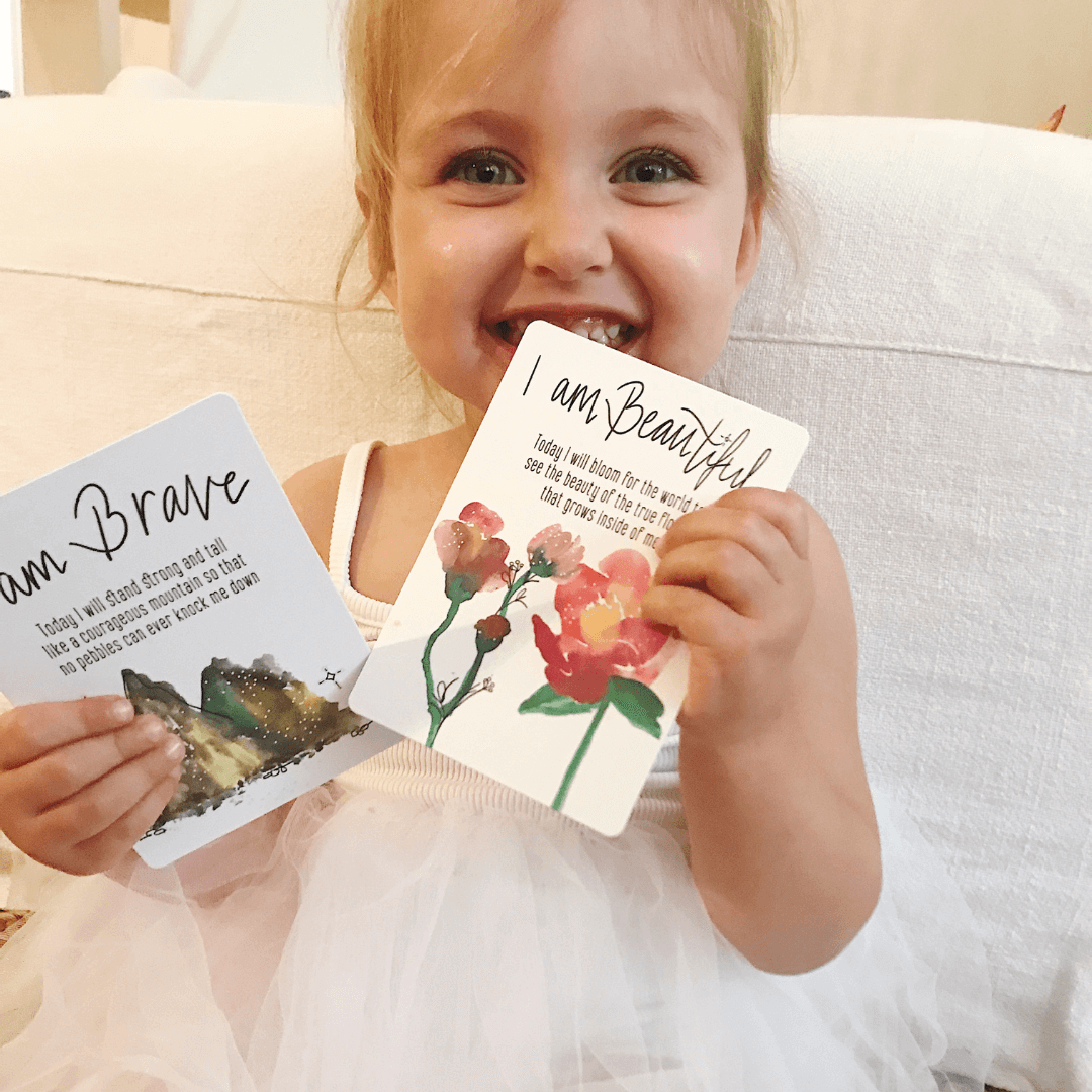 Child holding two affirmation cards with motivational phrases